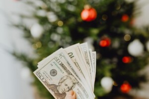 person holding dollar bills with christmas tree in background to save money