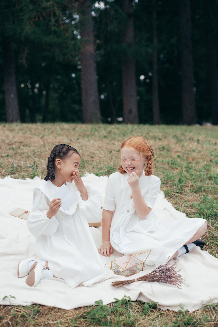 laughing girl friends sitting on white textile on green grass