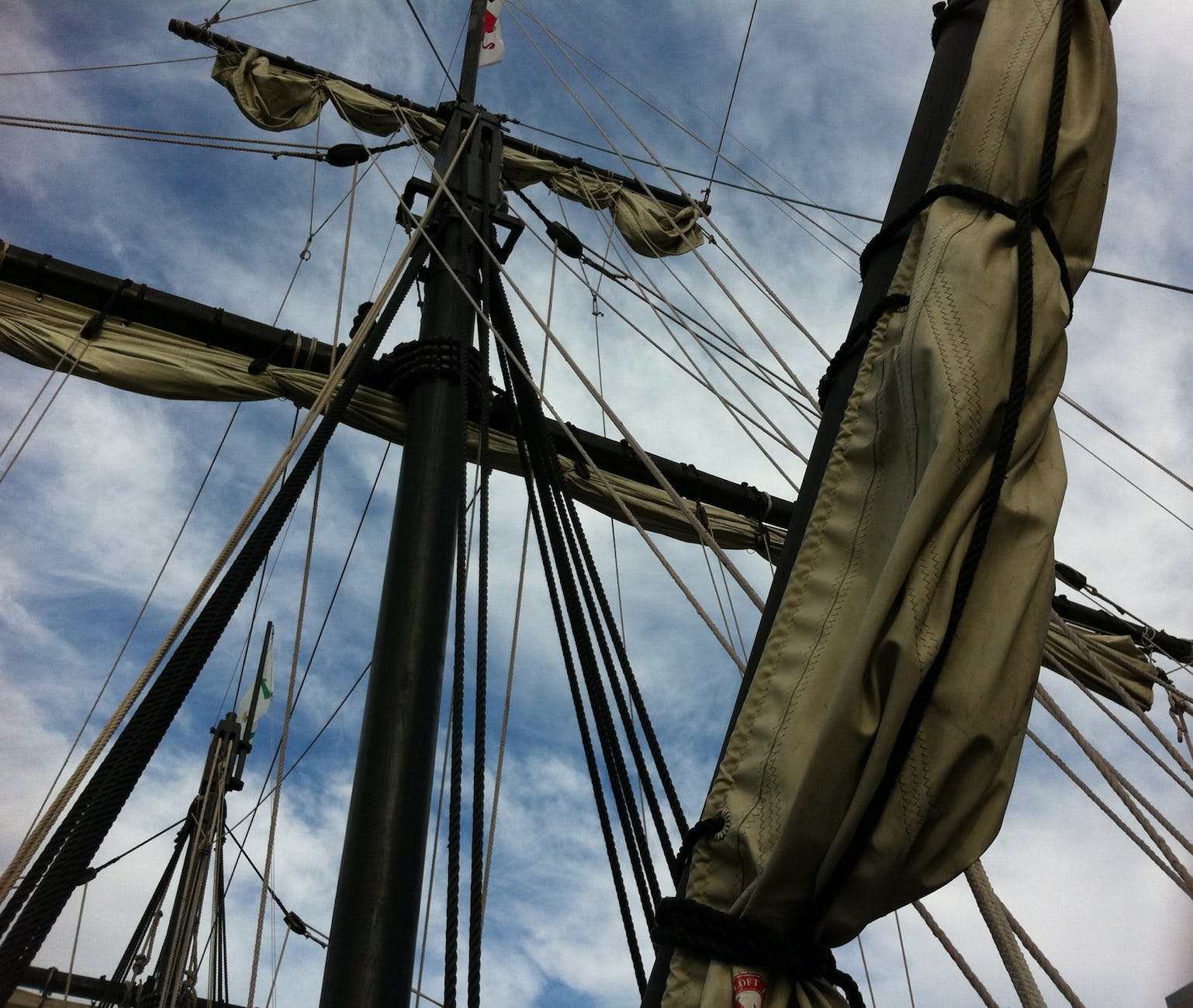 low angle photography of rolled up sails on ship under cloudy sky