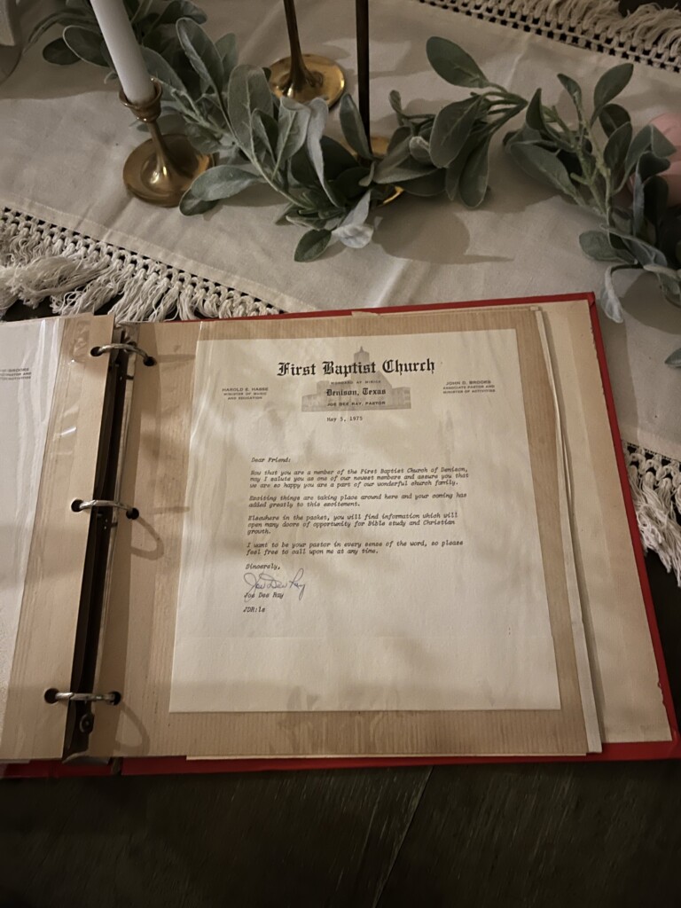 An open photo binder with a document titled "How to Preserve and Pass Down Your Family History" is displayed on a table, surrounded by a decorative table runner, candles, and foliage.
