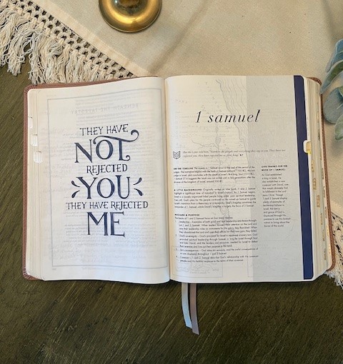 Open book on a table displaying two pages; the left page features a life applications quote saying "they have not rejected you, they have rejected me" and the right page begins the book of 1 Samuel.