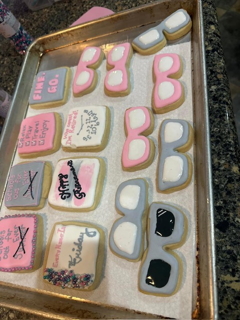 A tray of decorated cookies, some with sunglasses-shaped icing and others with messages like "Fine, go," and "In memory of my sleep." Perfect for a retirement party, the cookies are mostly in pastel colors like pink, purple, and white. Sprinkles adorn some of the cookies.